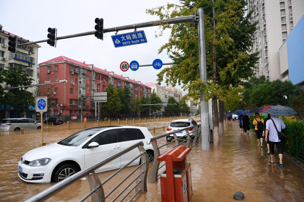 2023年7月31日，在北京市门头沟区大峪南路，行人从积水的路面和泡水的车辆旁走过。新华社记者鞠焕宗 摄